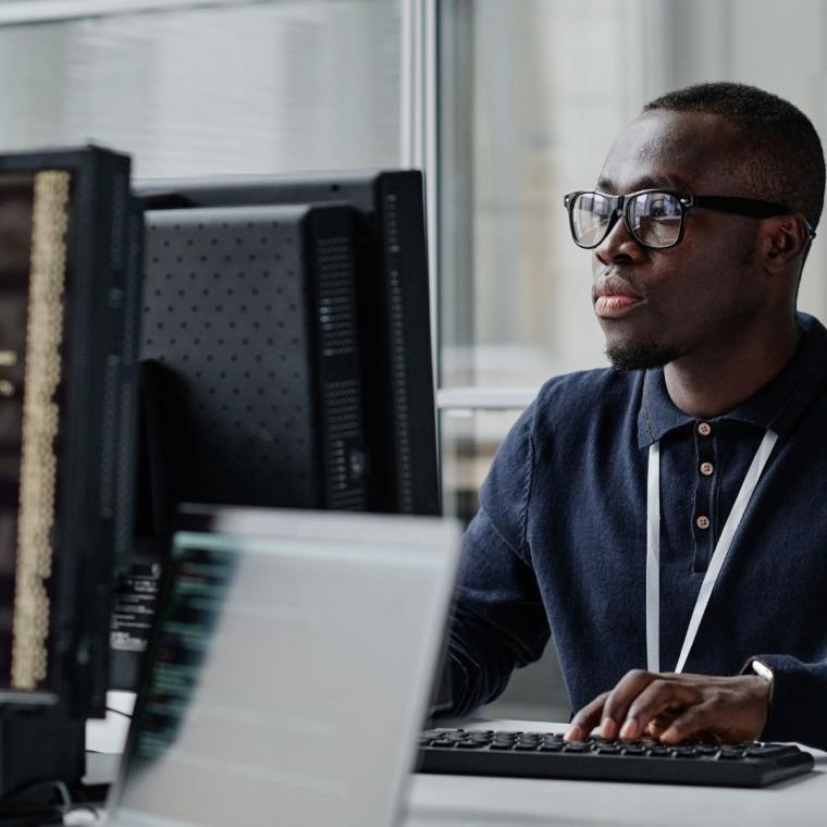 African American young developer in eyeglasses concentrating on his online work on computer sitting at workplace