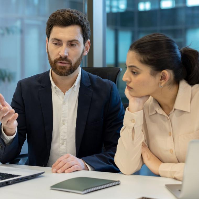 A business team is engaged in a discussion, looking at a laptop in a modern office environment.