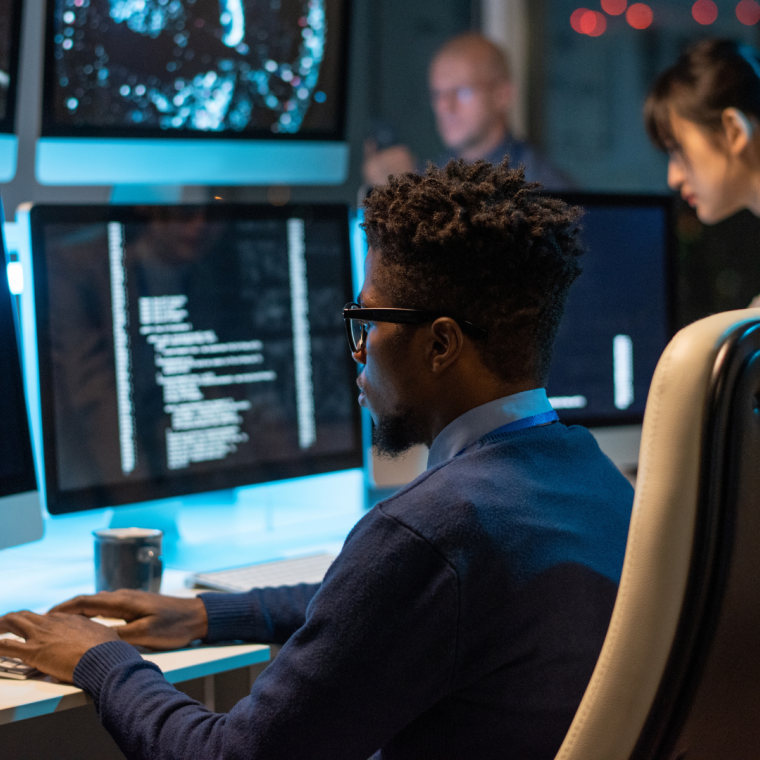 Young it-engineer decoding data while sitting in front of computer monitors and looking at screen of one of them 