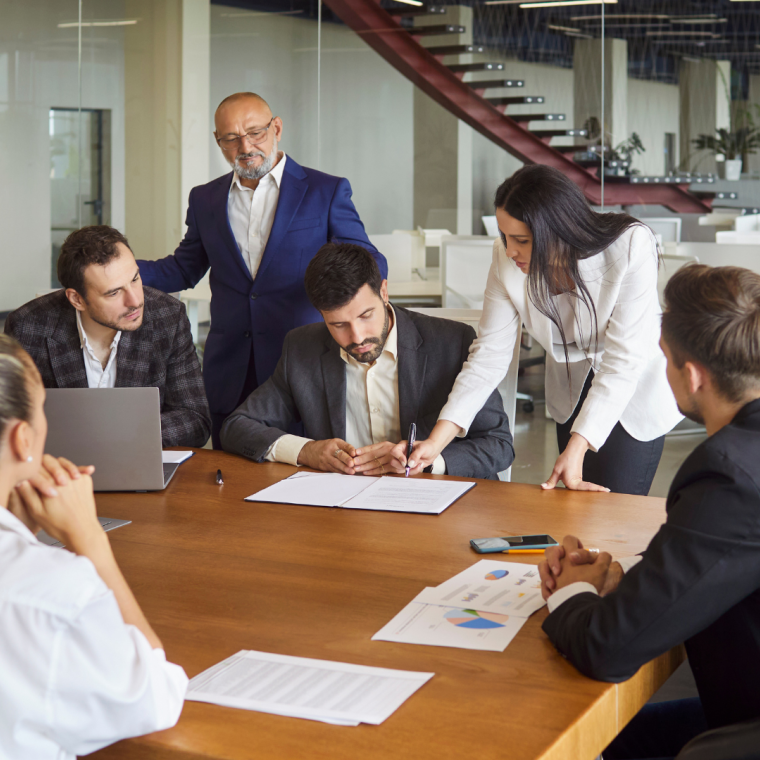 Business meeting for contract signing and discussion by corporate team in modern office. Businesswoman holding pen to sign document and approve agreement with diverse group of colleagues