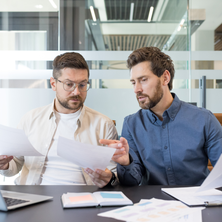Two business colleagues working together, discussing documents and analyzing data during a corporate meeting in a contemporary office setting, demonstrating teamwork and partnership