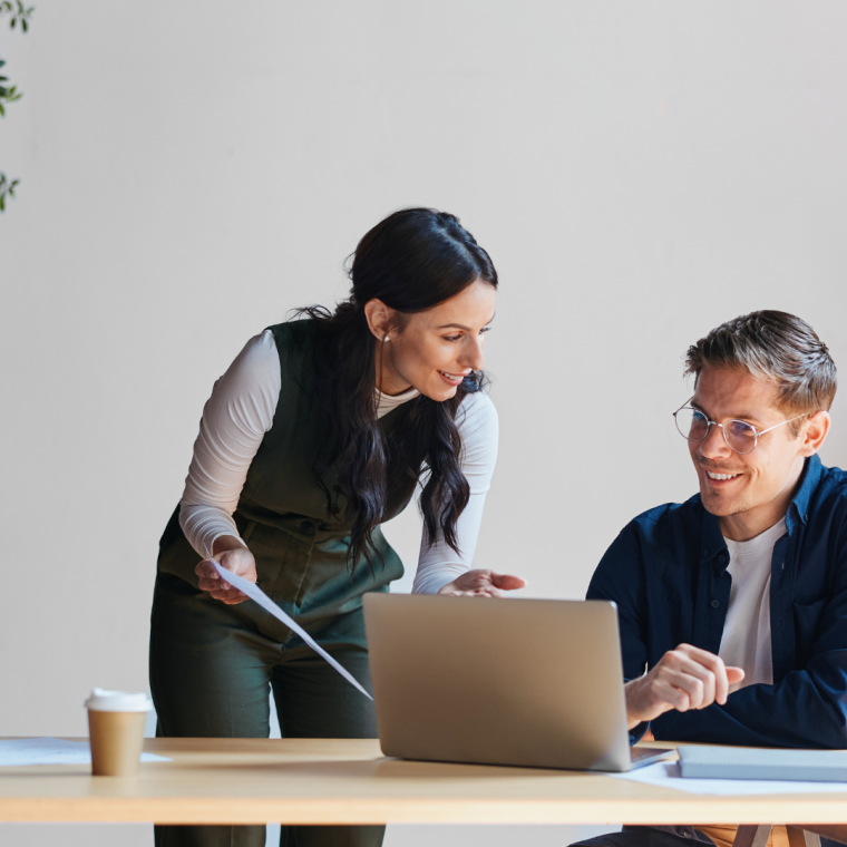 Business professionals collaborating at office desk, discussing project on laptop and documents, sharing ideas during meeting, working together in modern workspace