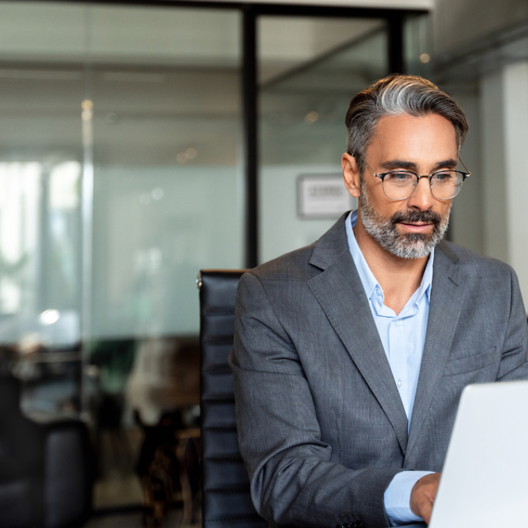 Happy mature European business man ceo trader using computer, typing, working in modern office, doing online data market analysis, thinking planning tech strategy looking at laptop with copy space.