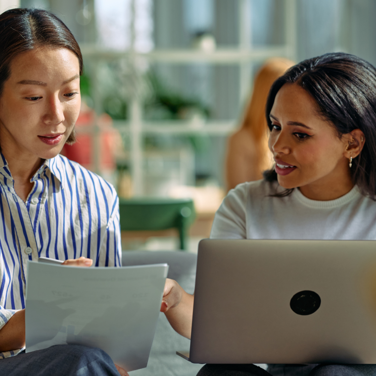 Businesswomen collaborating on project, discussing documents and laptop