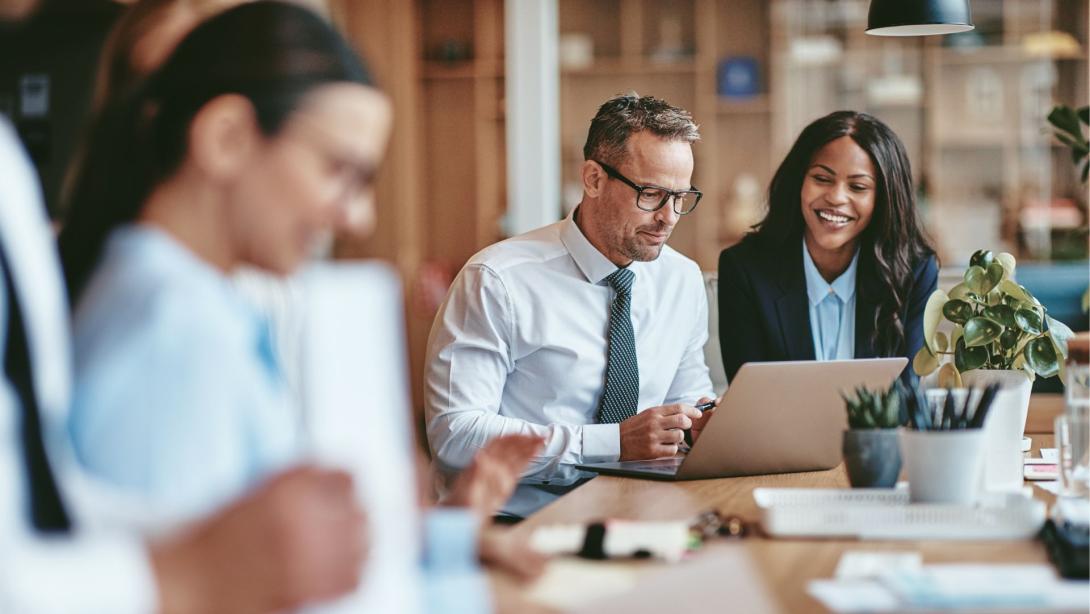 Two smiling diverse businesspeople using a laptop together at work