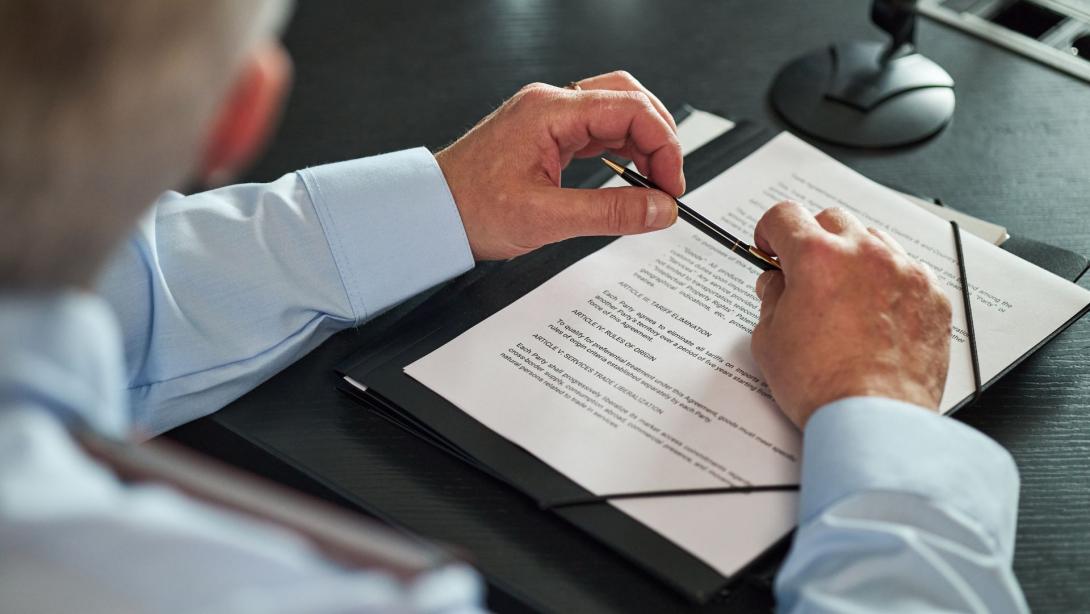 man sitting at desk reviewing official documents, holding pen in hands