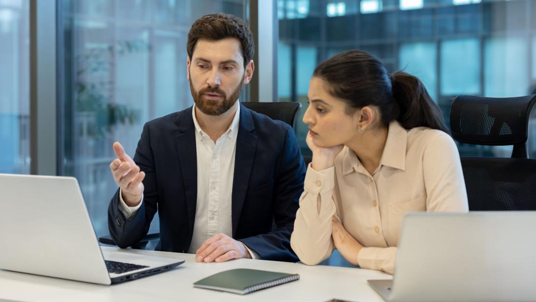 A business team is engaged in a discussion, looking at a laptop in a modern office environment.