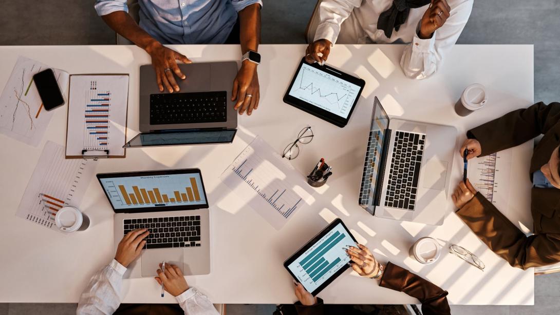 Team working with graphs and data on laptops and tablets at office table
