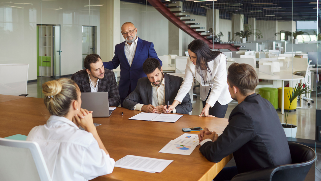 Business meeting for contract signing and discussion by corporate team in modern office. Businesswoman holding pen to sign document and approve agreement with diverse group of colleagues