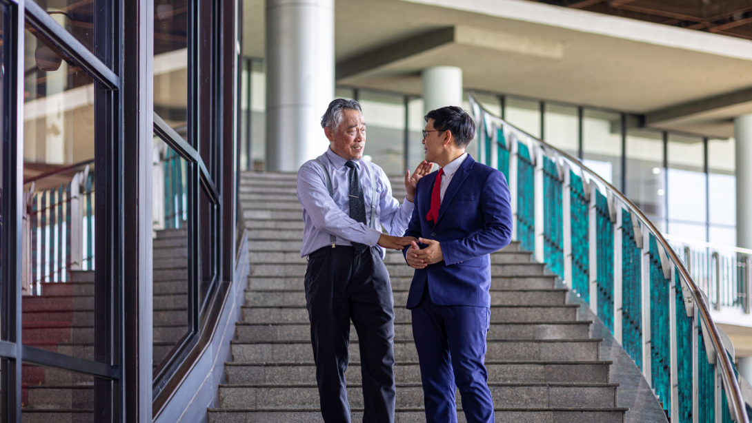 Meeting of two generations between senior and young business men at the company stairways sharing vision for their business development. Diversity and social inclusion in a business entrepreneurship