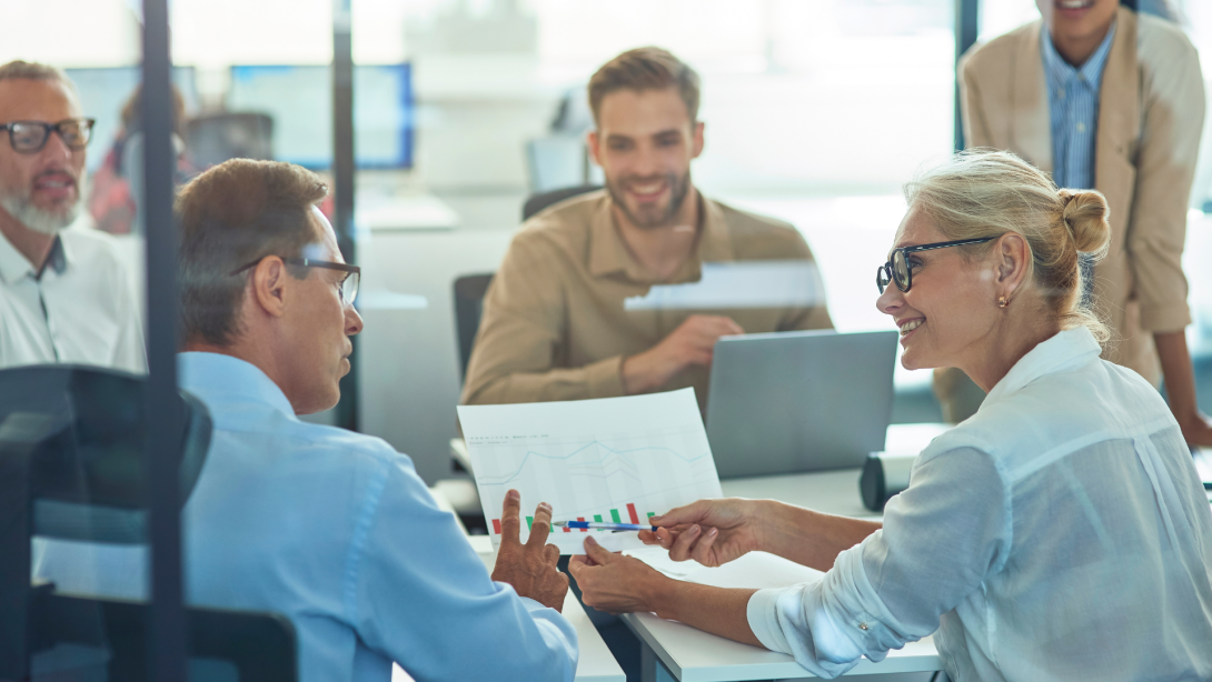 Beautiful mature business woman and her male colleague analyzing report and discussing results while having a meeting with project team 