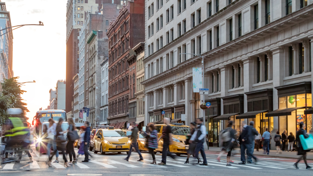Fast paced street scene with people walking across a busy intersection on Broadway in Manhattan New York City 