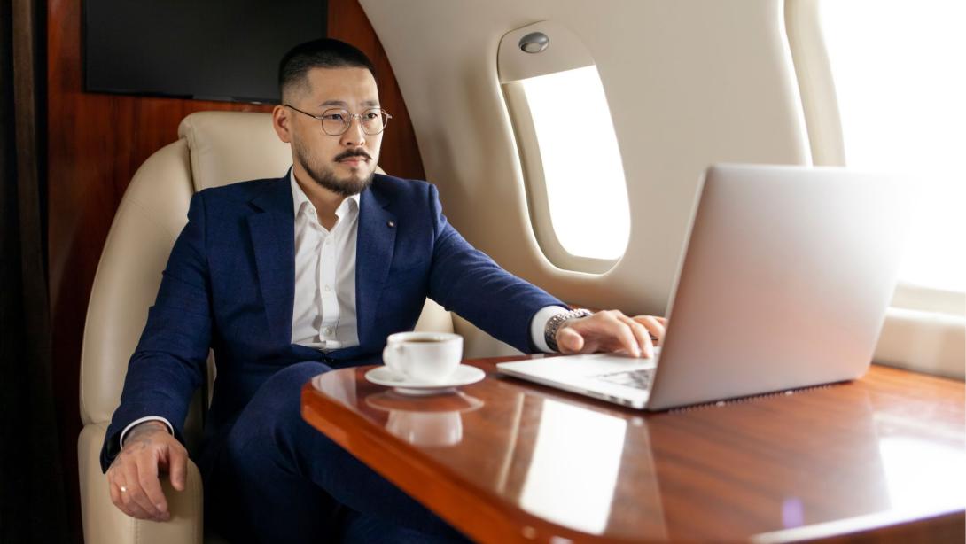 successful Asian businessman in suit and glasses flies in private luxury plane with laptop