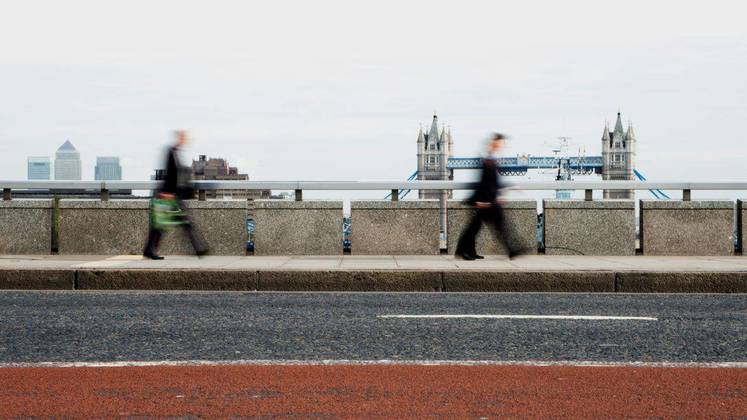 London Rush Hour: Business commuters, blurred by motion, walking along London Bridge with Tower Bridge in the background.