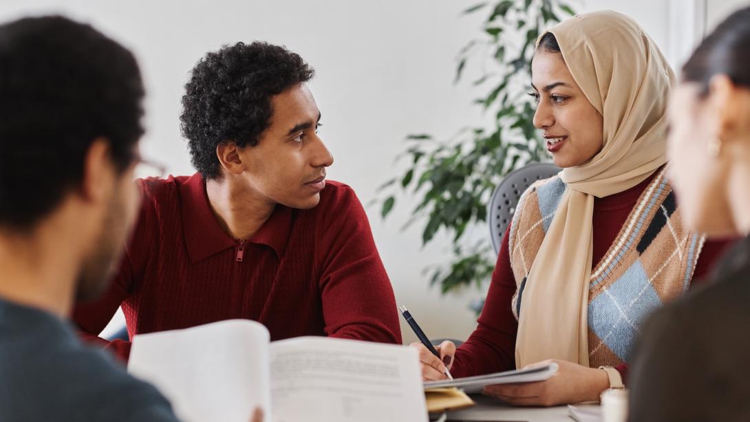 Group of modern Middle Eastern business people working together at meeting table in office and holding documents
