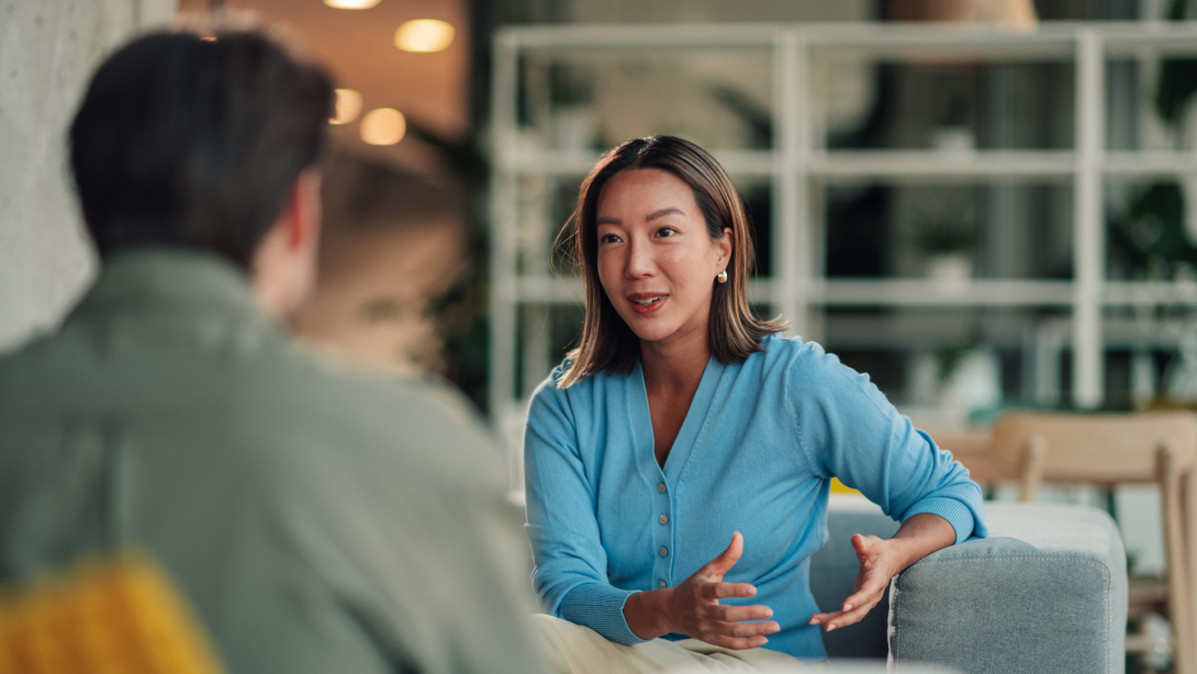 Asian businesswoman communicating with male colleague, discussing project, collaborating in modern office lounge 