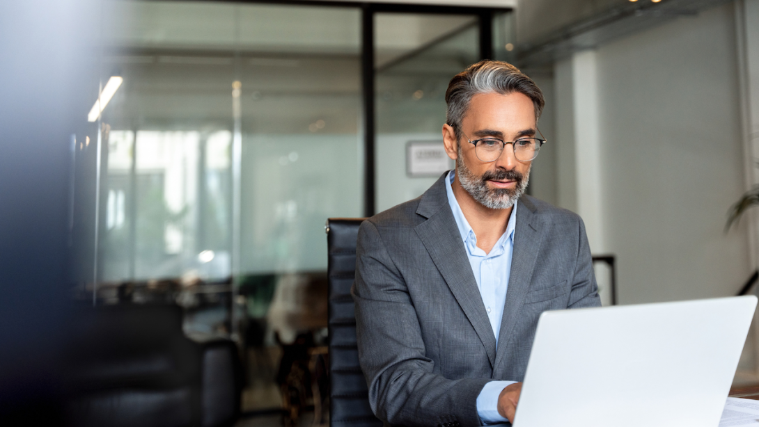 Happy mature European business man ceo trader using computer, typing, working in modern office, doing online data market analysis, thinking planning tech strategy looking at laptop with copy space.