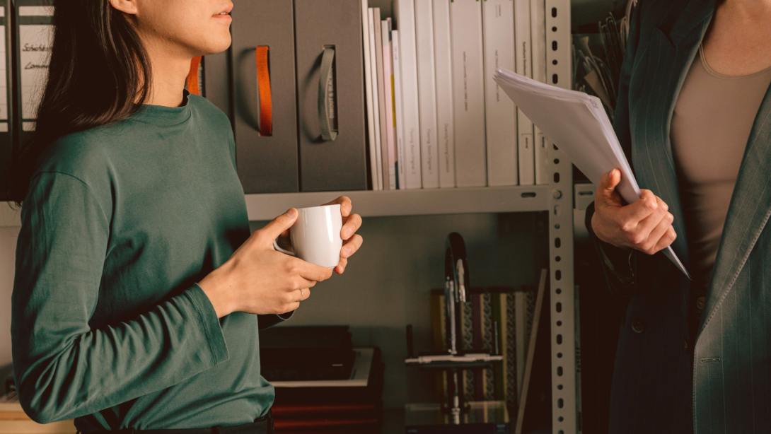 Two colleagues talking with a coffee in hand. 