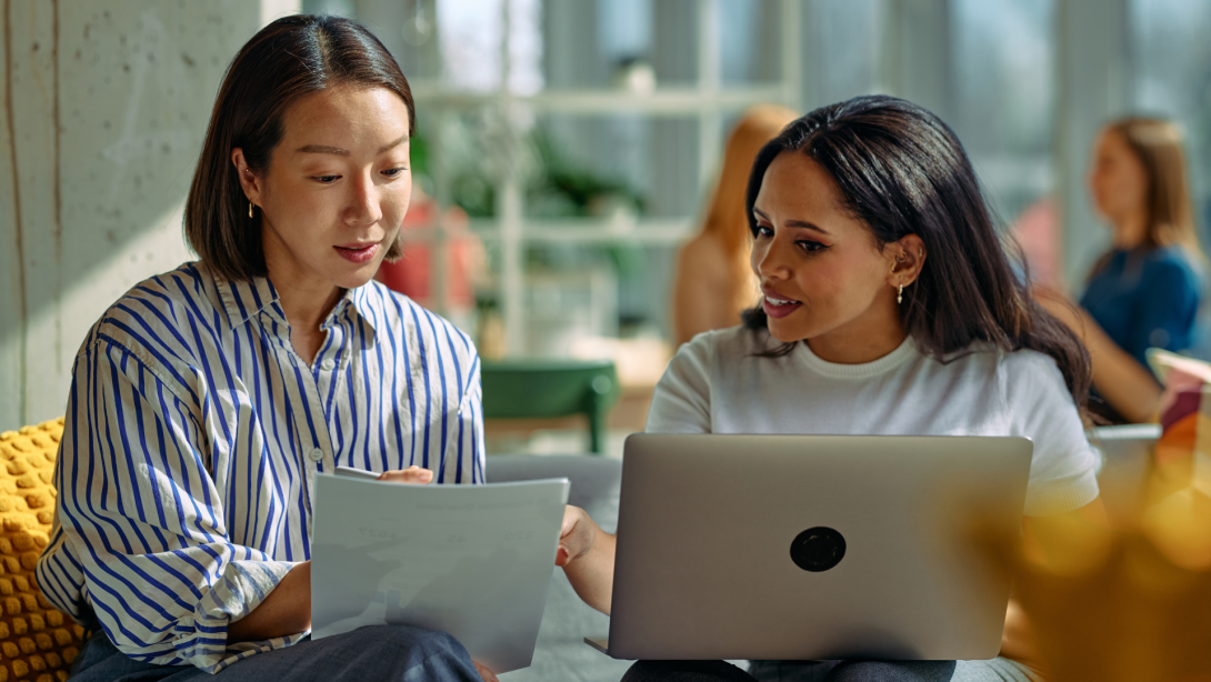 Businesswomen collaborating on project, discussing documents and laptop